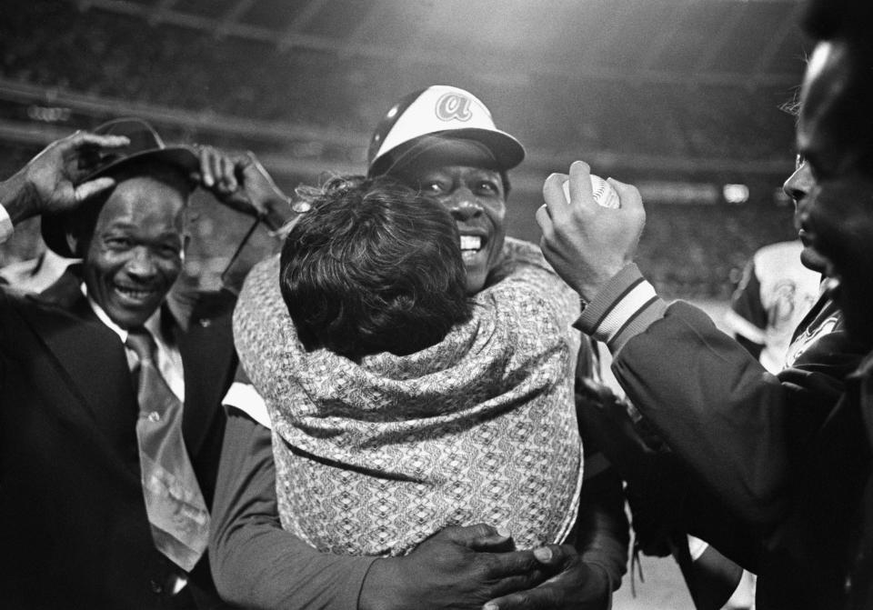 (Original caption) 8/4/1974-Atlanta, Georgia: Hank Aaron's mother gives her favorite home run hitter a hug after Hammerin'  Hank broke Babe Ruth's mark.  Connectó  A pitch from Dodgers pitcher Al Downing over the left-center field fence to record home run 715. On the right is the prized ball, held by Dodgers relief pitcher Tom House. Braves who captured heró  in the bullpen.