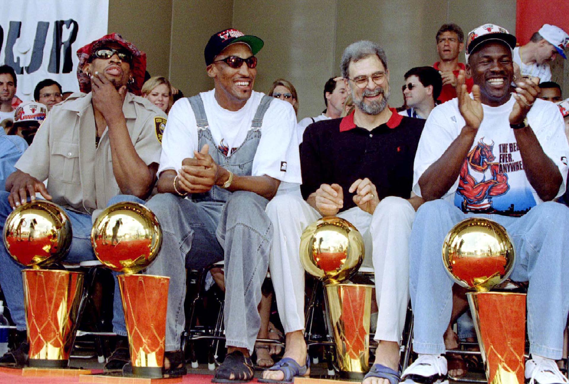 With their four championship trophies at their feet, Chicago Bulls Dennis Rodman (left), Scottie Pippen (left, center), coach Phil Jackson and Michael Jordan (right) laugh at a teammate's comments at a team rally in Chicago.