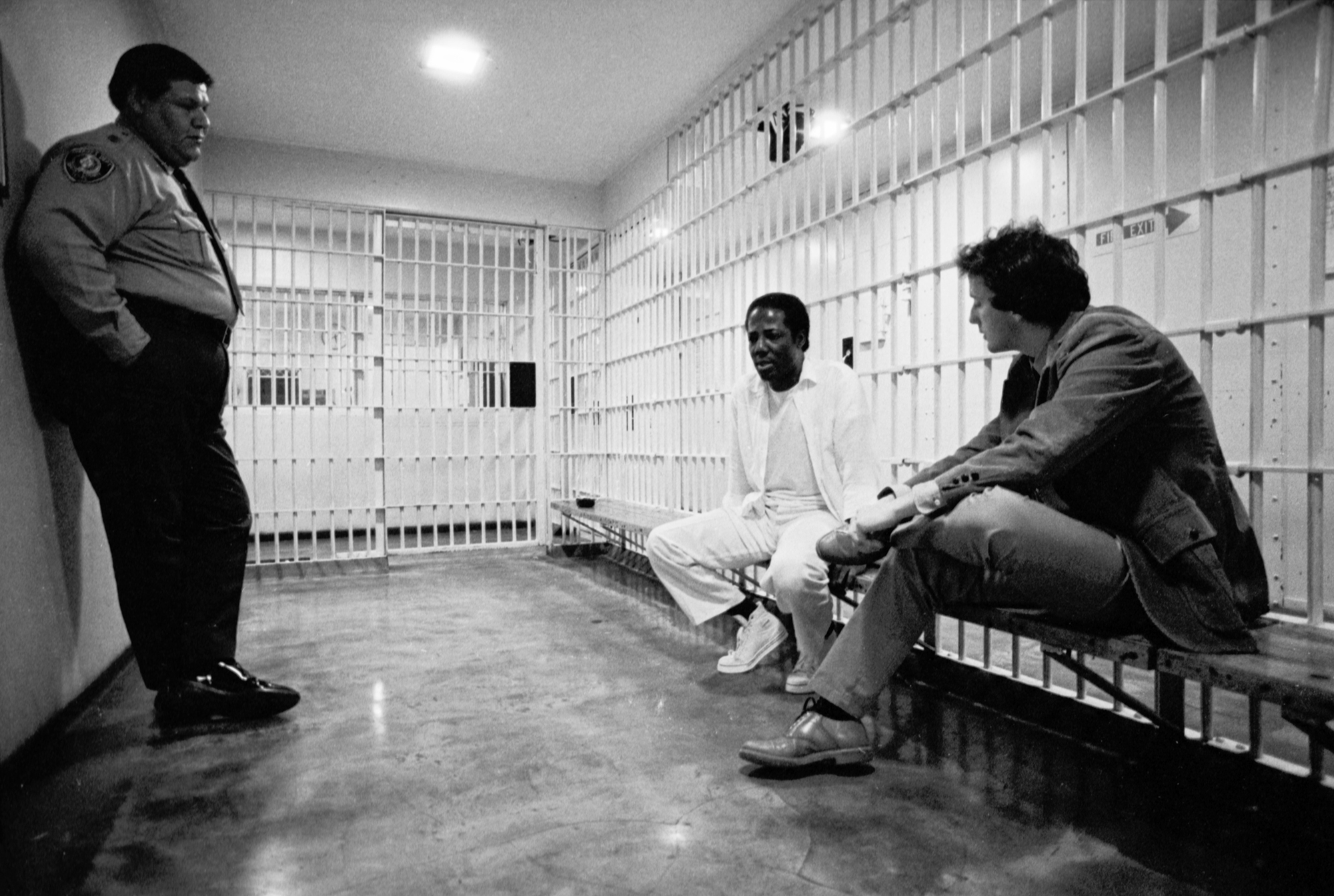 Charlie Brooks Jr., an inmate on death row at the Tarrant County Jail.  A prison guard is seen at left and Brooks is seen being interviewed by Fort Worth Star-Telegram reporter Jim Morris.  The clipping reads: "Brooks, 39, came within four days of being executed last December for the 1976 murder of used-car lot attendant David Gregory in Fort Worth.  A stay of execution issued by US District Judge David Belew, however, ensured that Brooks will not be put to death in the near future." [FWST photographer Rodger Mallison]